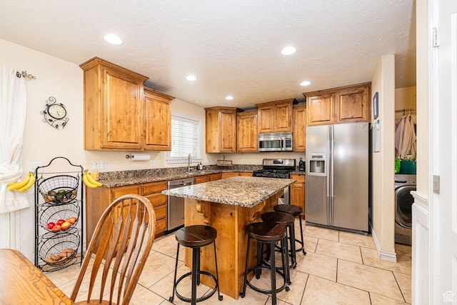 kitchen featuring appliances with stainless steel finishes, a sink, washer / dryer, brown cabinets, and light tile patterned floors
