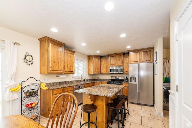 kitchen featuring stainless steel appliances, brown cabinetry, a breakfast bar, a kitchen island, and a sink