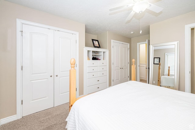 carpeted bedroom featuring two closets, ceiling fan, baseboards, and a textured ceiling