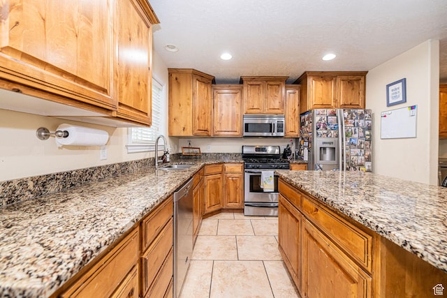 kitchen with appliances with stainless steel finishes, a sink, stone counters, brown cabinetry, and recessed lighting