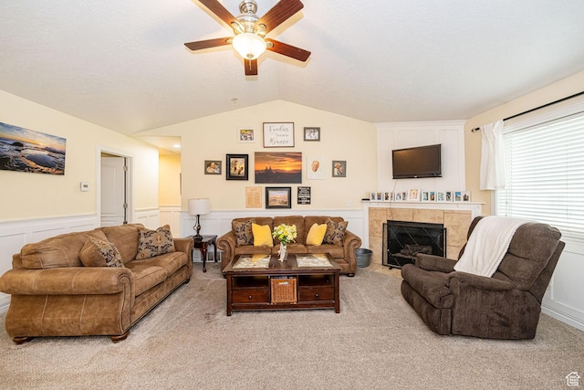 living area with vaulted ceiling, a ceiling fan, wainscoting, light colored carpet, and a fireplace