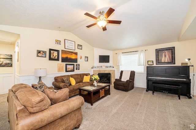 living area with ceiling fan, lofted ceiling, light carpet, a wainscoted wall, and a tile fireplace
