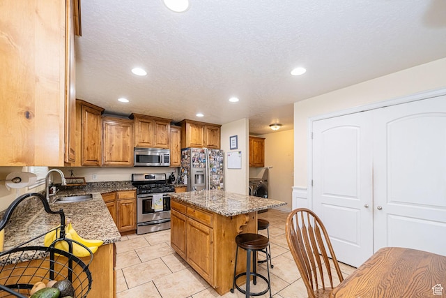 kitchen featuring stainless steel appliances, a sink, a kitchen breakfast bar, recessed lighting, and stone counters