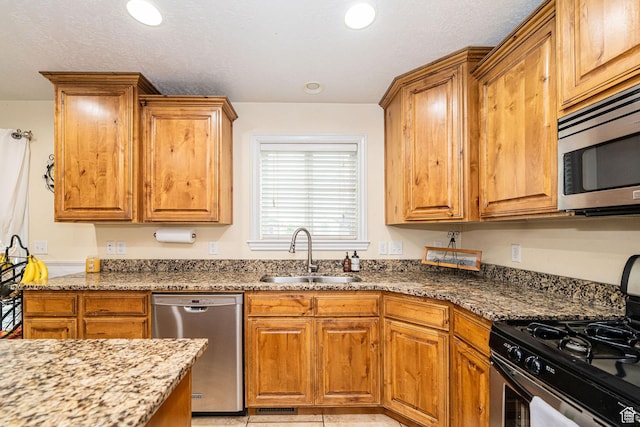 kitchen with appliances with stainless steel finishes, a sink, dark stone counters, brown cabinets, and recessed lighting