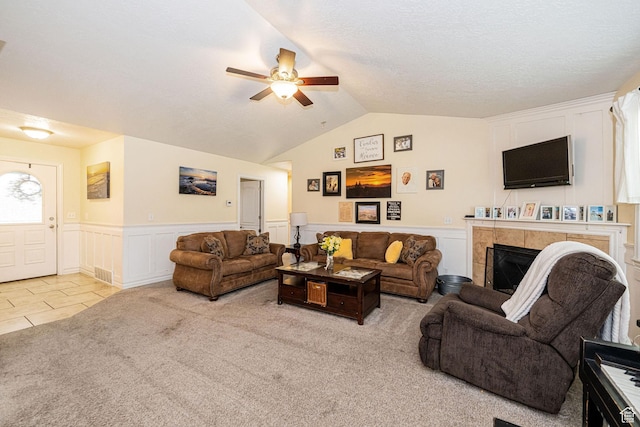 living area with a ceiling fan, light carpet, a wainscoted wall, lofted ceiling, and a fireplace