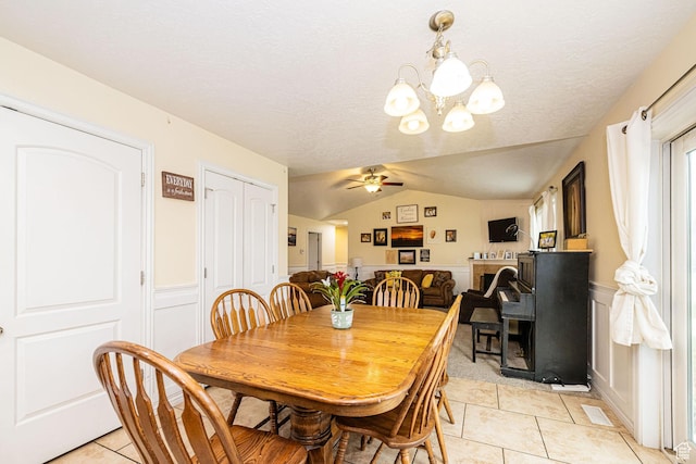 dining room featuring light tile patterned floors, a ceiling fan, a wainscoted wall, vaulted ceiling, and a chandelier