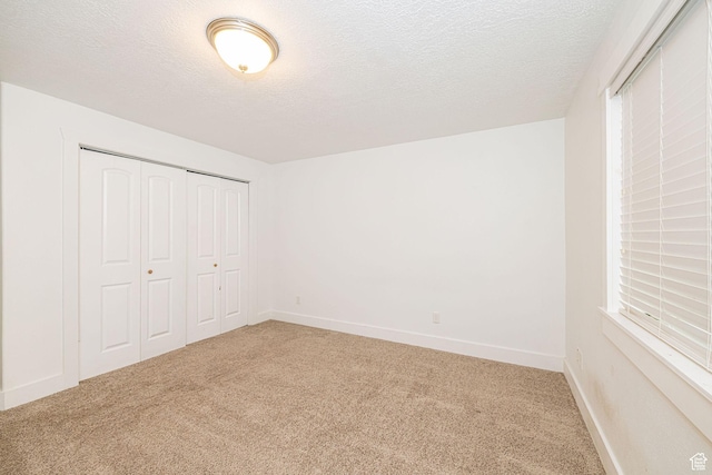 unfurnished bedroom with carpet, a textured ceiling, a closet, and baseboards