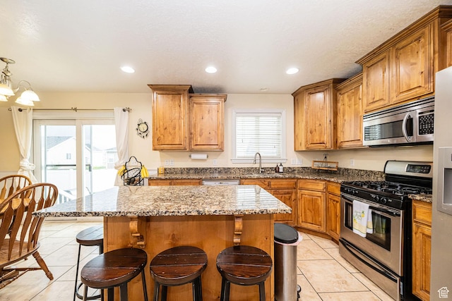 kitchen with stainless steel appliances, light tile patterned floors, a sink, a breakfast bar, and a kitchen island