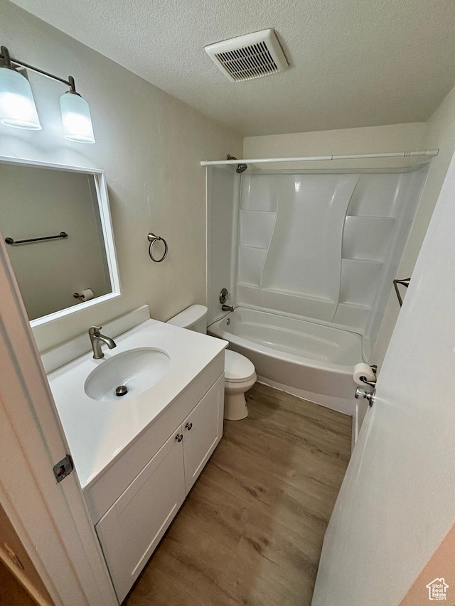 full bathroom with wood finished floors, toilet, a textured ceiling, vanity, and shower / tub combination