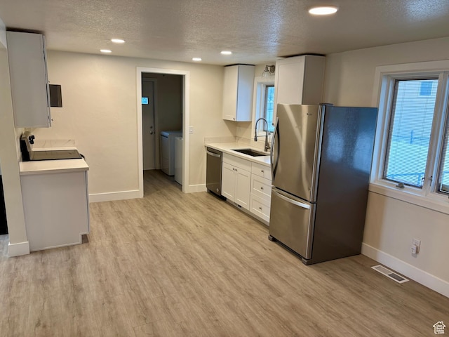 kitchen featuring appliances with stainless steel finishes, a sink, washer and dryer, a textured ceiling, and baseboards