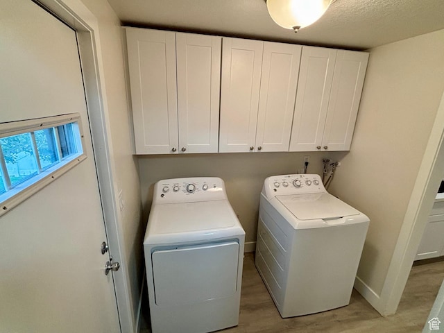 washroom with cabinet space, washing machine and dryer, light wood finished floors, and baseboards