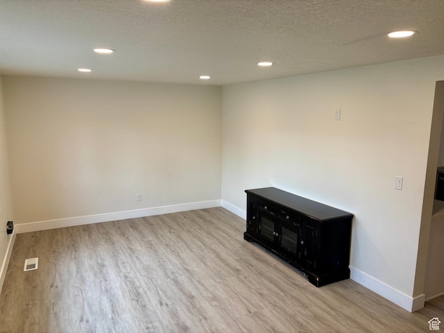 empty room with wood finished floors, recessed lighting, baseboards, and a textured ceiling