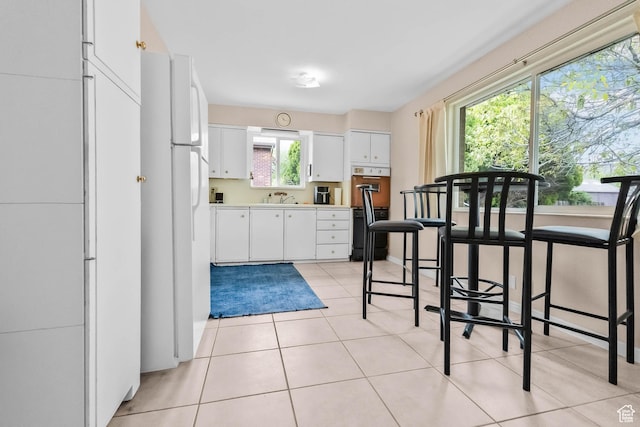 kitchen featuring white cabinetry, freestanding refrigerator, light countertops, light tile patterned floors, and a sink