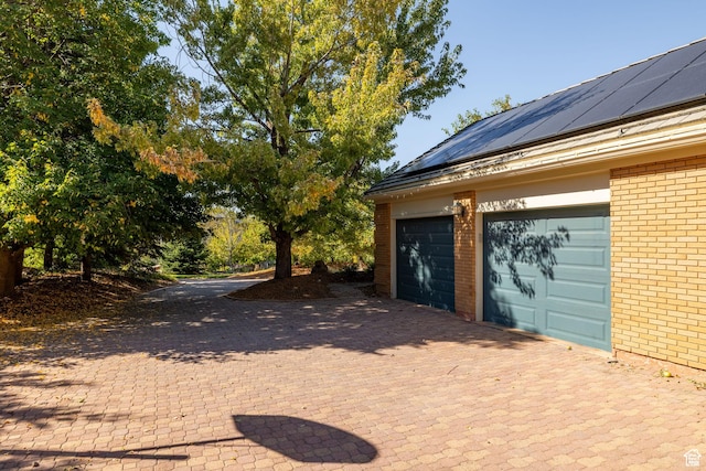garage featuring roof mounted solar panels and decorative driveway