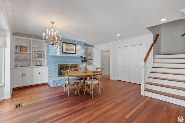 dining area featuring wood finished floors, stairs, a chandelier, a brick fireplace, and ornamental molding