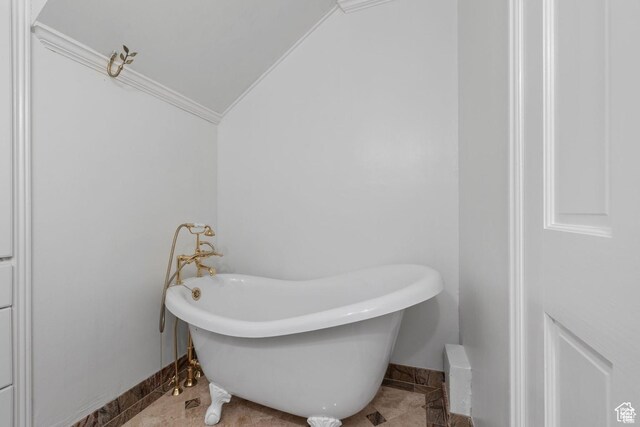 bathroom with lofted ceiling, a freestanding tub, ornamental molding, baseboards, and tile patterned floors