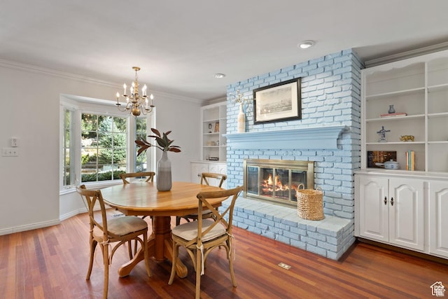 dining area with wood finished floors, a chandelier, a fireplace, ornamental molding, and baseboards