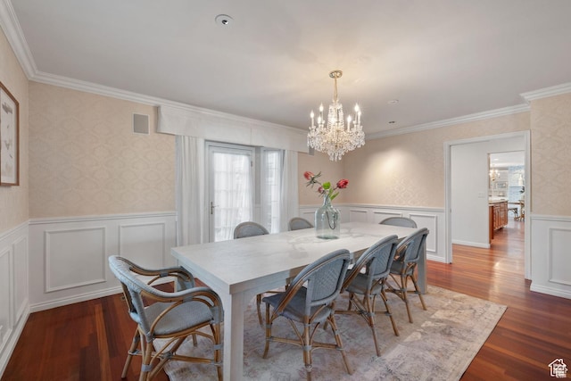 dining room with a chandelier, wood finished floors, ornamental molding, wainscoting, and a decorative wall