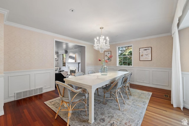 dining area featuring a chandelier, a lit fireplace, crown molding, wainscoting, and wood finished floors