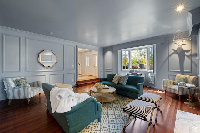 living area with a decorative wall, wood finished floors, and ornamental molding