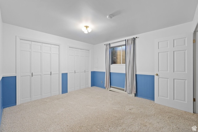 unfurnished bedroom with two closets, carpet floors, and wainscoting