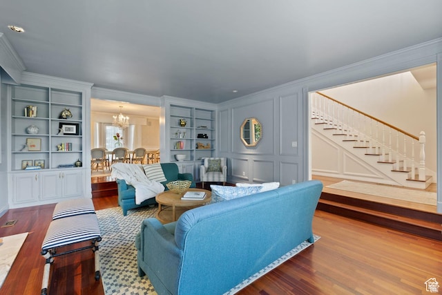 living area featuring crown molding, a chandelier, dark wood finished floors, stairs, and built in features