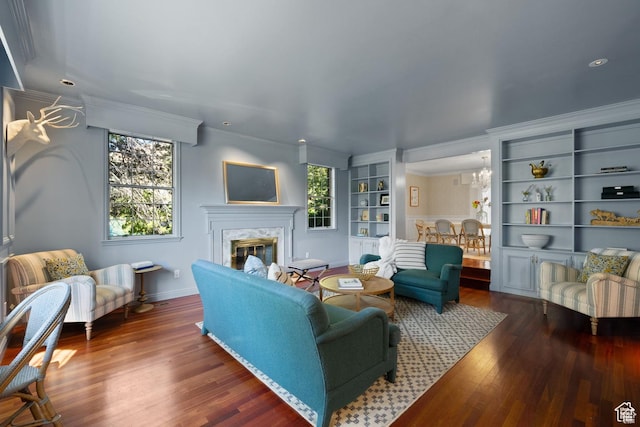 living room with wood finished floors, a premium fireplace, crown molding, baseboards, and a chandelier