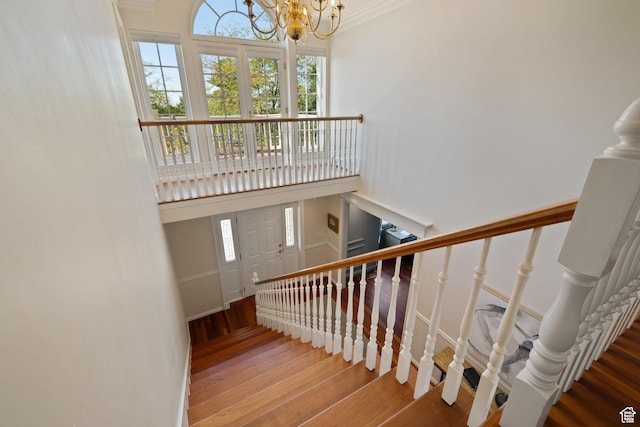 stairs featuring wood finished floors, a chandelier, healthy amount of natural light, a high ceiling, and crown molding