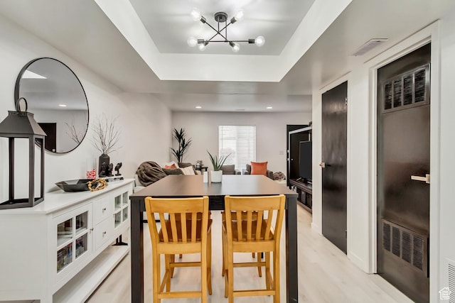 dining room with a chandelier, light wood finished floors, a raised ceiling, and a heating unit