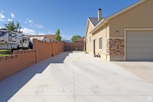 view of home's exterior featuring stucco siding, fence, stone siding, concrete driveway, and a chimney