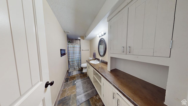full bathroom with stone tile floors, toilet, vanity, a shower with curtain, and a textured ceiling