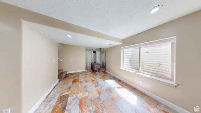unfurnished living room featuring a wood stove, baseboards, light stone finish floors, a textured ceiling, and recessed lighting