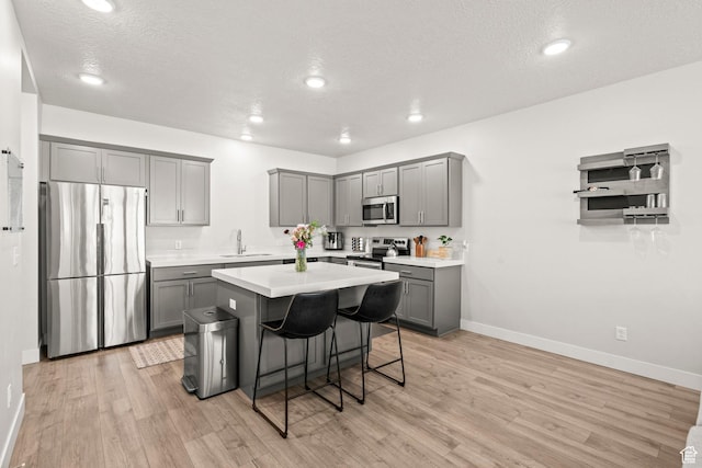 kitchen featuring appliances with stainless steel finishes, gray cabinetry, a sink, baseboards, and a textured ceiling