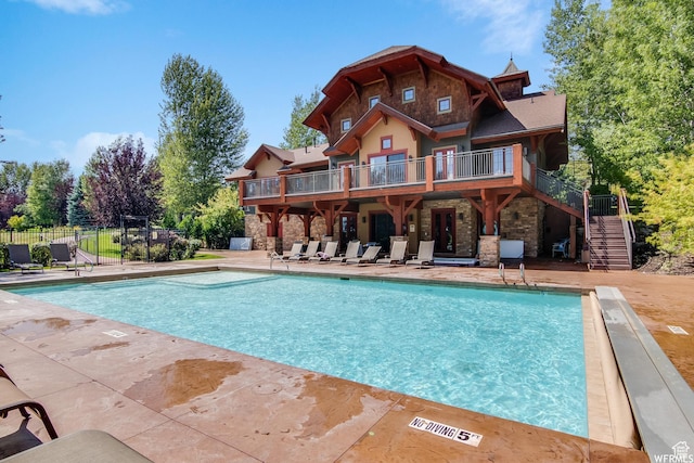 rear view of property with stone siding, a community pool, a patio, stairway, and fence