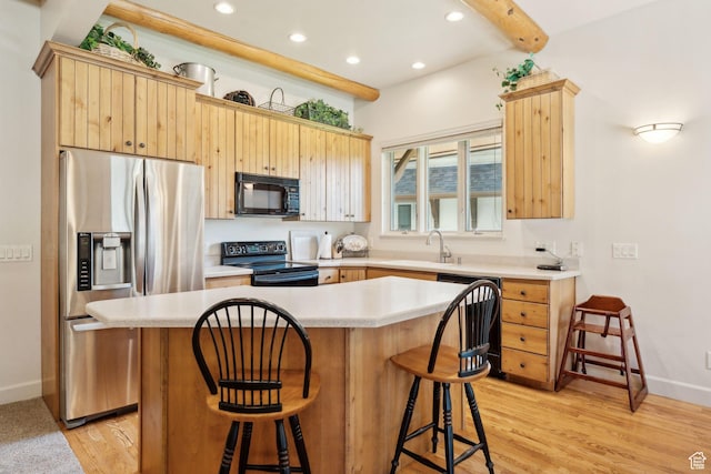kitchen featuring black appliances, a sink, light brown cabinetry, a kitchen bar, and recessed lighting