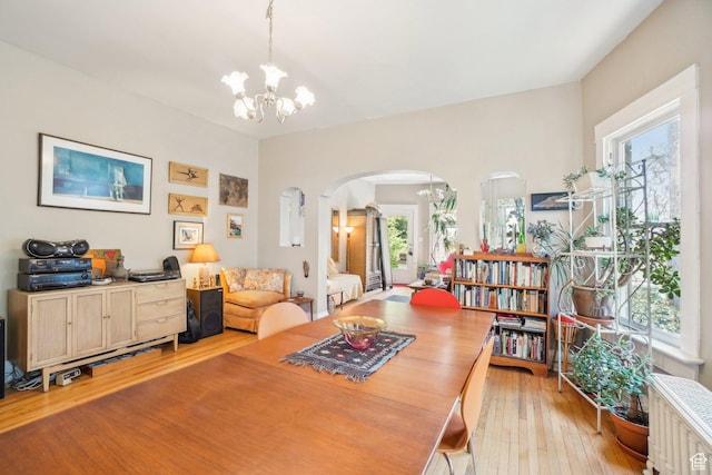 dining room featuring a chandelier, arched walkways, light wood-type flooring, and radiator
