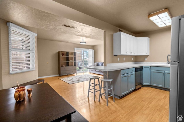 kitchen featuring appliances with stainless steel finishes, a peninsula, light wood-type flooring, a breakfast bar, and white cabinetry