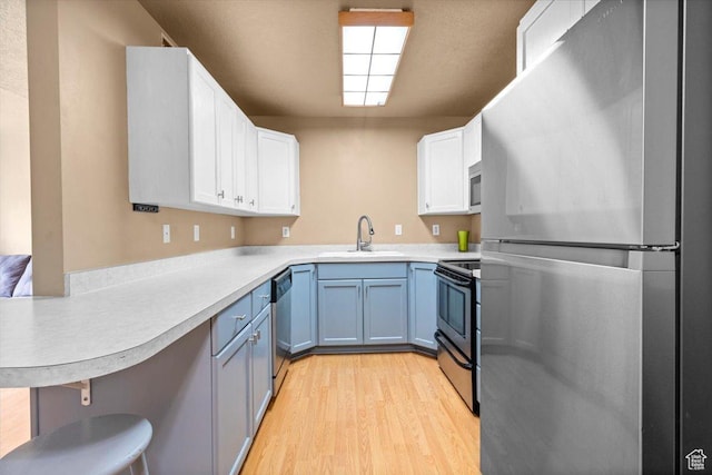 kitchen featuring appliances with stainless steel finishes, a sink, light wood-type flooring, a peninsula, and white cabinets