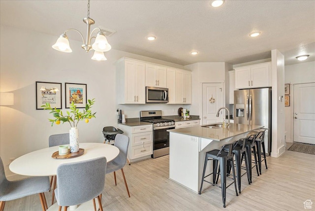 7881 S Highlandpoint Way, West Jordan, UT 84081 - kitchen with stainless steel appliances, a sink, a breakfast bar area, light wood-style flooring, and an island with sink