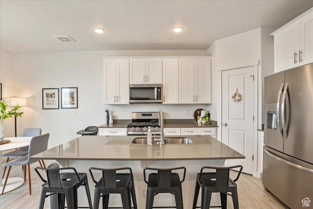 7881 S Highlandpoint Way, West Jordan, UT 84081 - kitchen with stainless steel appliances, a sink, a breakfast bar area, light wood-type flooring, and white cabinets