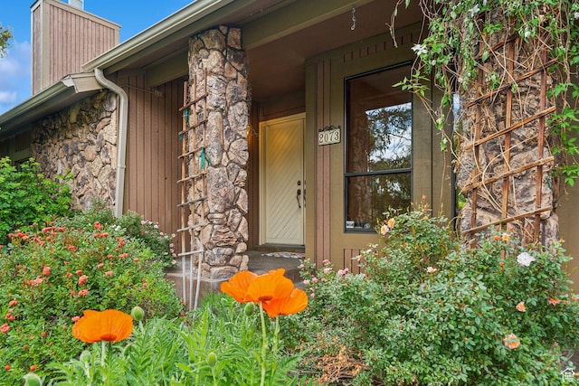 doorway to property with stone siding, a chimney, and covered porch