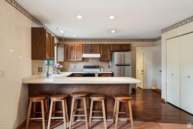 kitchen with electric range, a sink, freestanding refrigerator, under cabinet range hood, and light countertops