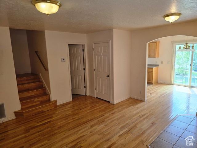 834 N Sapphire St, Morgan, UT 84050 - unfurnished living room with arched walkways, light wood-style floors, a textured ceiling, stairs, and a chandelier