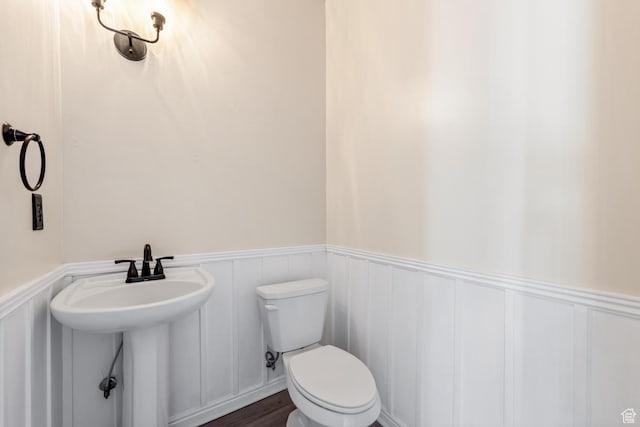 bathroom with toilet, a wainscoted wall, a decorative wall, and wood finished floors