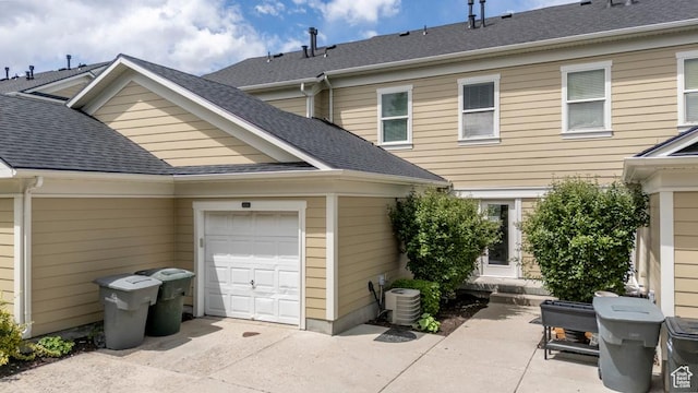 view of side of property with an attached garage, concrete driveway, roof with shingles, and cooling unit
