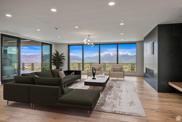 living area with expansive windows, a mountain view, light wood-style flooring, a glass covered fireplace, and recessed lighting