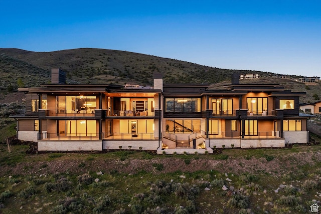 back of house at dusk featuring a chimney, a mountain view, and a balcony