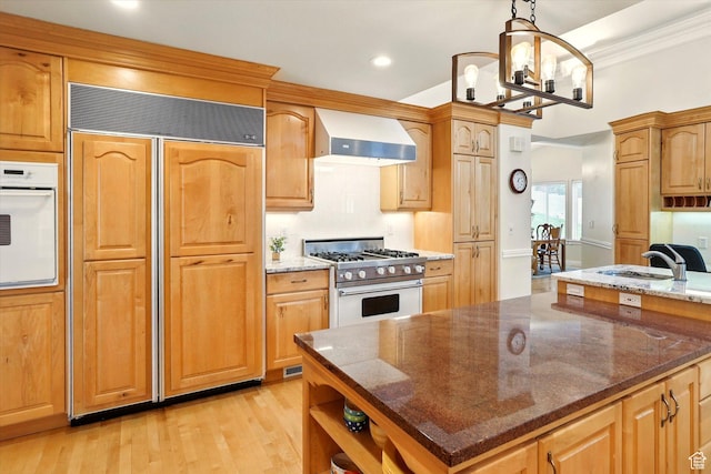 kitchen with wall chimney range hood, high quality appliances, a sink, light wood-style flooring, and dark stone countertops