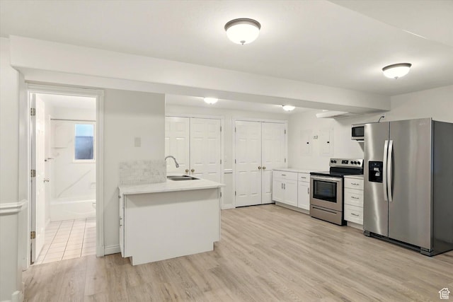 kitchen featuring appliances with stainless steel finishes, a sink, light wood-style floors, light countertops, and a peninsula