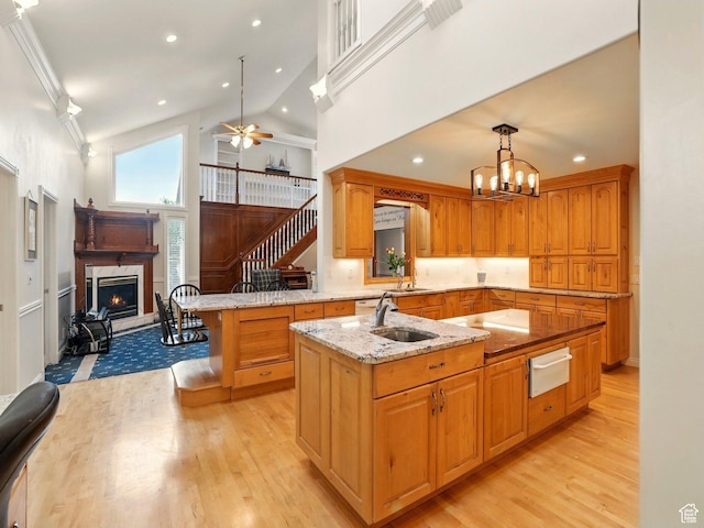 kitchen featuring a lit fireplace, a warming drawer, a sink, light wood finished floors, and high vaulted ceiling